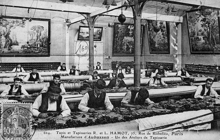 Un atelier de tissage de tapisserie à Aubusson, appartenant à la société Hamot (présente à Felletin). Les lissiers sont au travail. L'alignement systématique et le nombre important de métiers montrent la rationalisation et la concentration du travail effectives dès la 2e moitié du 19e siècle dans un secteur d'activité pourtant encore caractérisé par une mise en oeuvre manuelle.