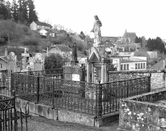 Monument sépulcral comportant une grande dalle entourée d'une clôture en en fer et surmontée de deux stèles ornées chacune d'une statue.