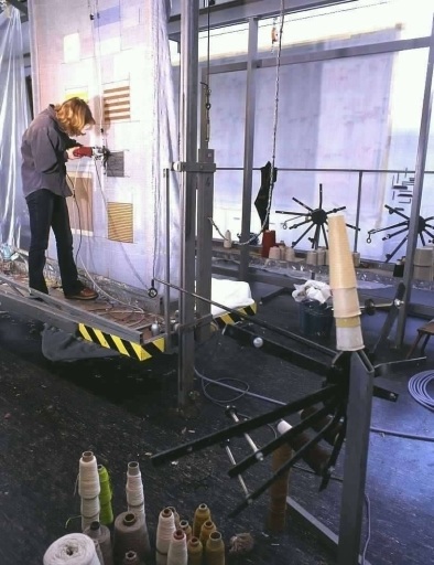 Réalisation d'échantillons de tapis 'hand-tuft'. Sur une toile de coton, tendue à l'aide d'un métier vertical, une ouvrière implante à l'aide d'un pistolet à laine, le velours formant le duvet du tapis. La cohésion avec la toile est ensuite assurée par un encollage. Au premier plan à droite, un ourdissoir, appareil qui, relié au pistolet, fournit la laine.