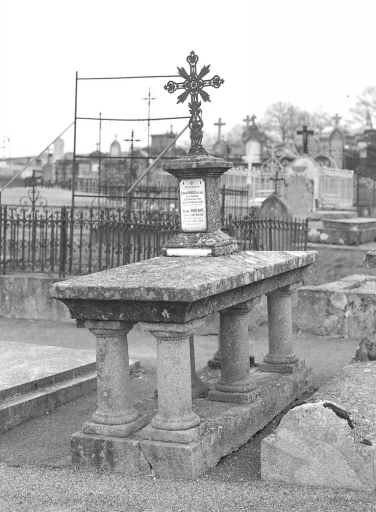 Tombe n° 9 : tombe de l'abbé Coudert. Tombe en granite supportée par six pieds en forme de colonne et surmontée d'une stèle ornée d'une plaque émaillée et d'une croix en métal. Vue d'ensemble.