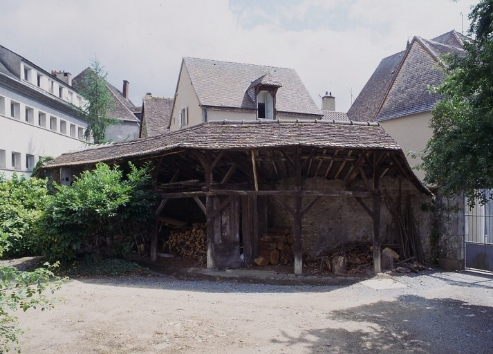 Vue d'un hangar (peut-être remise à chevaux), adossé au mur de clôture de la cour et dont la couverture en tuile creuses repose sur des poteaux en bois.