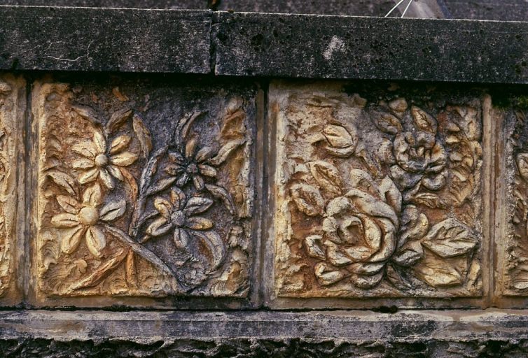 Tombe n° 16. Tombe ornée de plaques réalisées en ciment armé, à la manière des rocailleurs et représentant un décor floral. Détail d'une plaque.