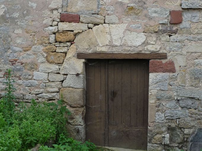 Porte droite percée dans l'embrasure d'une ancienne porte en arc en plein-cintre donnant accès à l'étage de soubassement et à la cave voûtée.