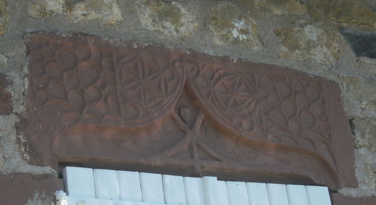 Détail d'un linteau en grès orné d'un arc en accolade se terminant par une fleur de lys encadré par deux rosaces et orné d'un motif de résille.
