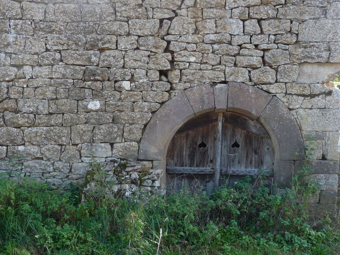 Leygonie. Maçonnerie en blocage de moellons de calcaire. Encadrement de porte en pierre de taille de grès rouge. ; Porte en arc en plein-cintre donnant accès à la cave voûtée.