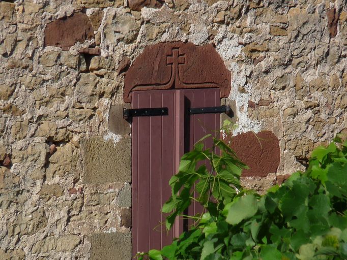 Mur de croupe nord du logis : fenêtre à linteau en grès orné d'un arc en accolade se terminant par une croix, en remploi.