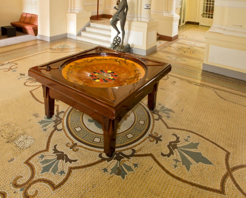 Vue du décor de mosaïque du hall initial du casino : le monogramme CL (casino Luchon) prend place au centre, sous la table à jeux.