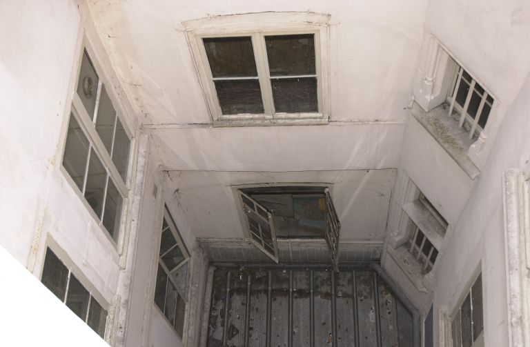 Cour orientale vue depuis le haut de l'escalier principal ; galeries au fond, pan coupé de l'escalier en vis à droite.