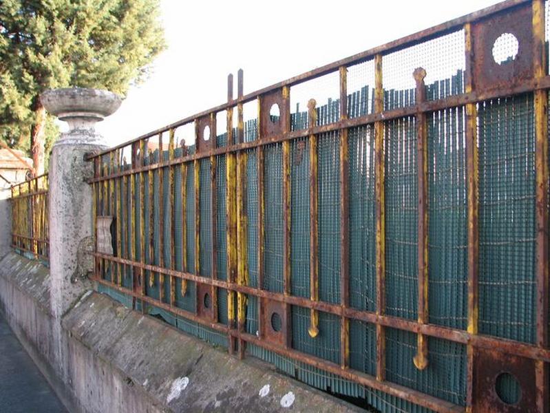 Clôture : muret surmonté d'une grille en ferronnerie rythmée par des colonnes surmontées d'un vase