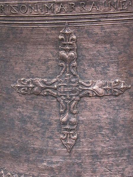 Cloche (n°1), détail de plaquettes avec caractères, une grande croix grecque aux bras ondulés, extrémités en forme de fleur de lys, bras formés par des coeurs et des volutes adossées, au centre IHS (lettres entrelacées).