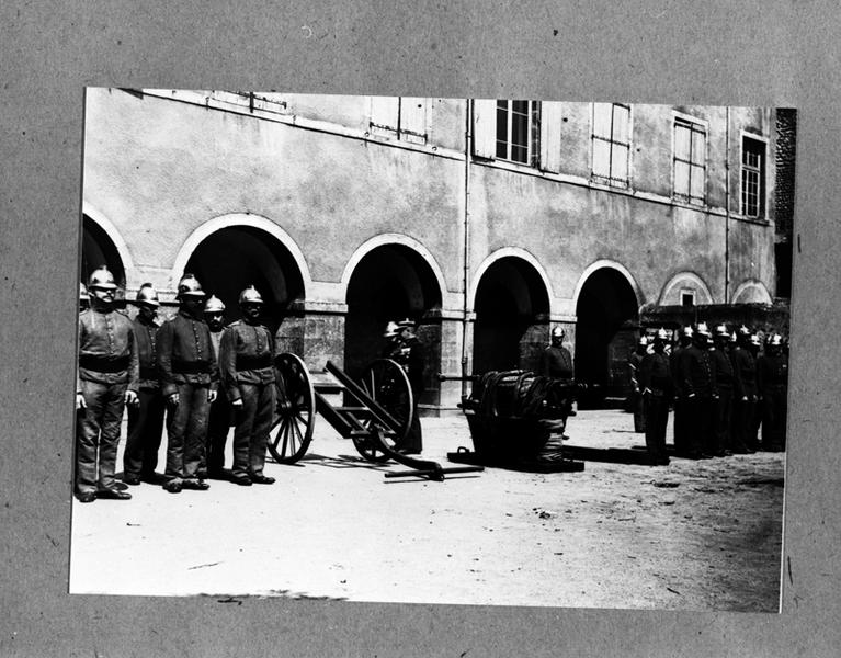 Inspection du corps des sapeurs pompiers de Maringues,dans la cour de la mairie,avec présentation d'une des pompes à incendie et de son chariot,photographie sur plaque de verre,vers 1900.(A.P.Maringues)