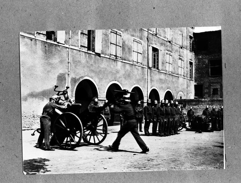 Inspection du corps des sapeurs pompiers de Maringues,dans la cour de la mairie,avec une des pompes à incendie en cours d'installation sur son chariot,photographie sur plaque de verre,vers 1900.(A.P.Maringues)