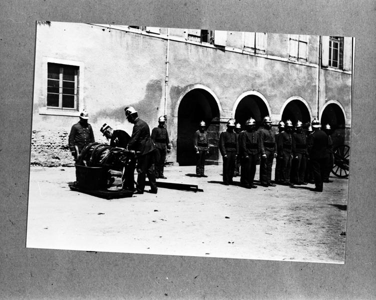 Inspection du corps des sapeurs pompiers de Maringues,dans la cour de la mairie,avec présentation d'une des pompes à incendie et de son chariot,photographie sur plaque de verre,vers 1900.(A.P.Maringues)