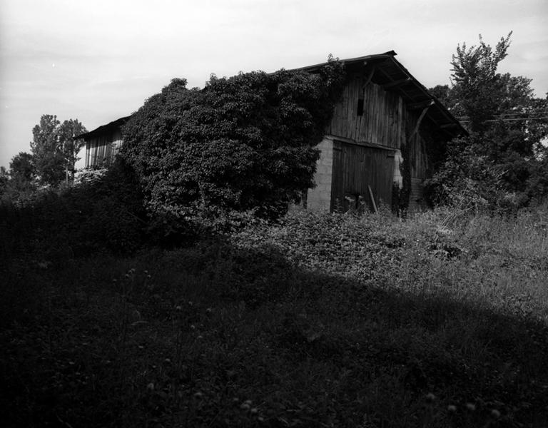 Vue générale d'une grange longitudinale à essentage de planches, avec entrée et avant-toit en mur pignon (Les Caires, Limons).
