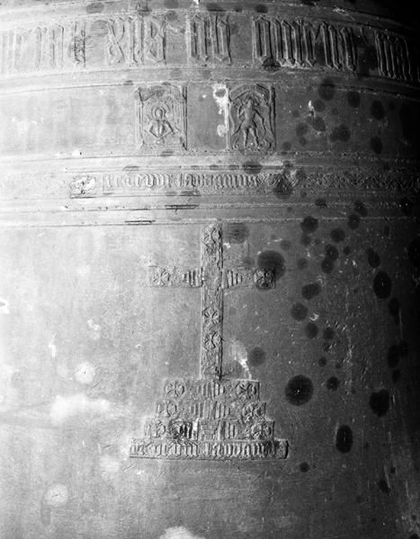 Cloche 1, décor de la face postérieure et vue partielle des deux lignes de l'inscription. Ligne 1 : XPS AB OMENI. Ligne 2 et marche inférieure de la grande croix : TE DEUM LAUDAMUS. Figures sur dossier : Christ de la messe de saint Grégoire et saint Michel.