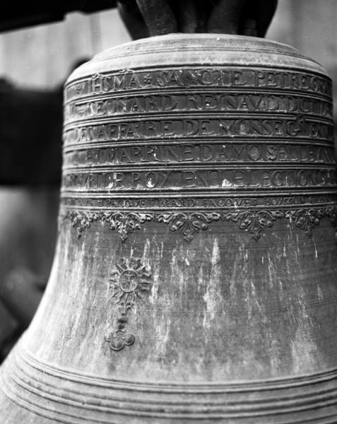 'Cloche 2, face antérieure, détail : sur le vase supérieur, les six lignes de l'inscription et la frise ; sur la faussure, ostensoir, l'hostie ornée d'un Calvaire'