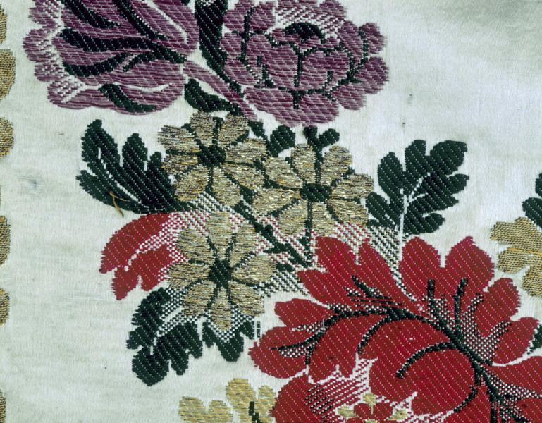 Voile d'exposition du Saint-Sacrement, détail : guirlande, bas, groupe de trois fleurs or après la grosse fleur rouge. Ombres produites sans dégradé de couleur, par des liages par découpure, seuls (broché vert ou rouge), ou par l'alternance, sur deux passées, d'un coup de filé or et d'un coup de broché rouge ou d'un coup de broché vert. Satin de 10, broché, à liage repris en sergé 4 lie 1 sens S par le sixième des fils.