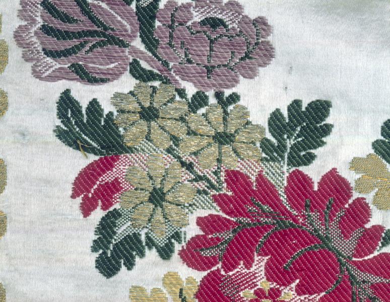 Voile d'exposition du Saint-Sacrement, détail : guirlande, bas, groupe de trois fleurs or après la grosse fleur rouge. Ombres produites sans dégradé de couleur, par des liages par découpure, seuls (broché vert ou rouge), ou par l'alternance, sur deux passées, d'un coup de filé or et d'un coup de broché rouge ou d'un coup de broché vert. Satin de 10, broché, à liage repris en sergé 4 lie 1 sens S par le sixième des fils.