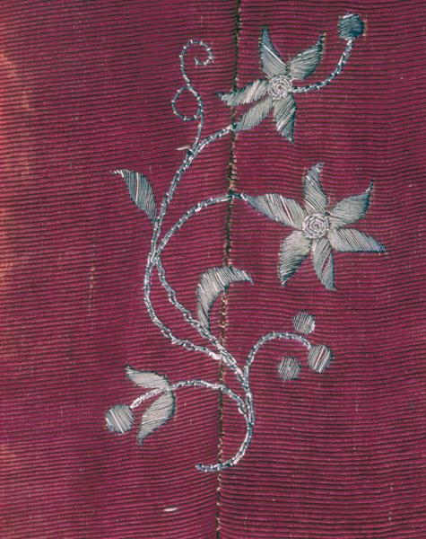 Chape, fond, détail : fleur brodée (second motif), filé argent sur cannelé rouge moiré, peut-être inspirée des narcisses. Le décor brodé chevauche une couture sens chaîne, et atteste ainsi d'un montage antérieur à la broderie.