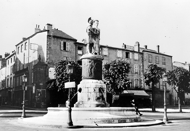 Vue générale de la fontaine Desaix et dans le fond un des piliers de la porte de Clermont