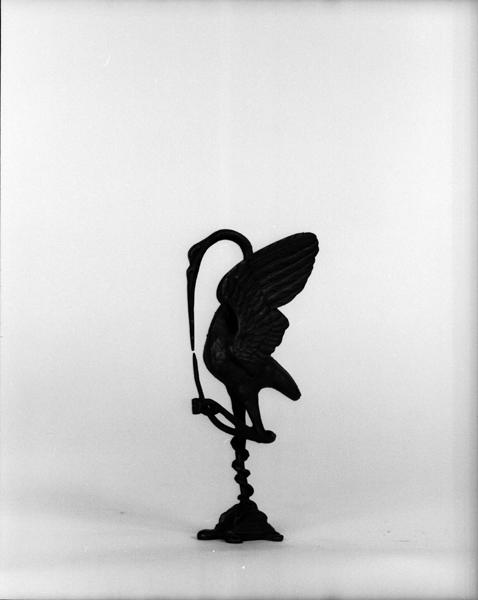 Détail d'une des deux cigognes traitées comme des amortissements des chandeliers. Toutes les deux enserrent un serpent qui s'enroule autour d'une de leur patte posée sur une tortue.