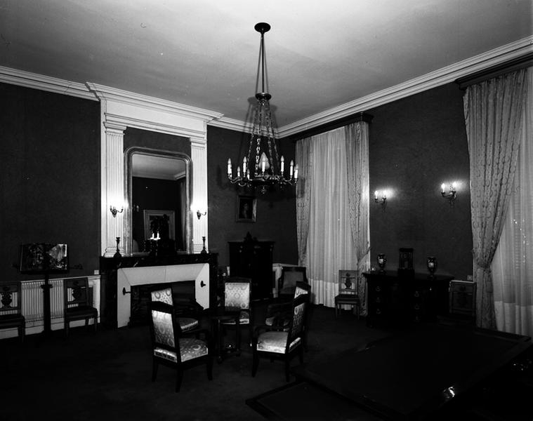 Bureau du Procureur général. Angle nord-est, avec bureau en premier plan, fauteuils autour d'une table en guéridon au-dessus desquels est suspendu le lustre, à droite : commode sur laquelle prennent place les vases et l'horloge, dans le fond : secrétaire à abattant.