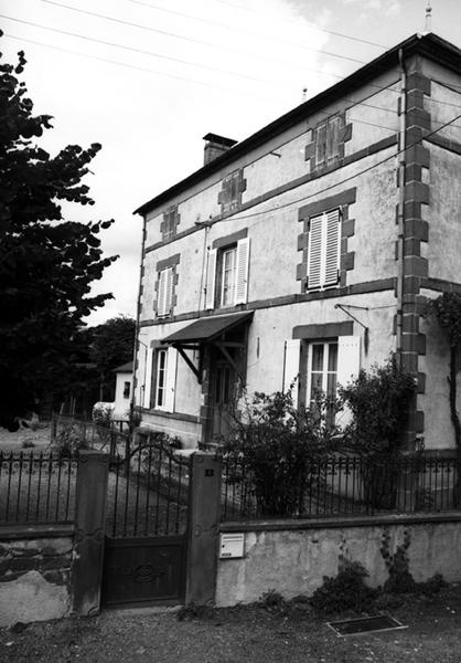 Vue de trois quarts de la façade du logis sur la cour. Au premier plan, le muret de clôture et la porte piétonne aux piles ornées.