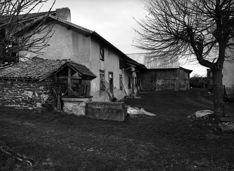 Vue de trois quarts de la maison-bloc à logis double. Au premier plan, le four à pain et le puits. A l'arrière plan, la grange-étable.