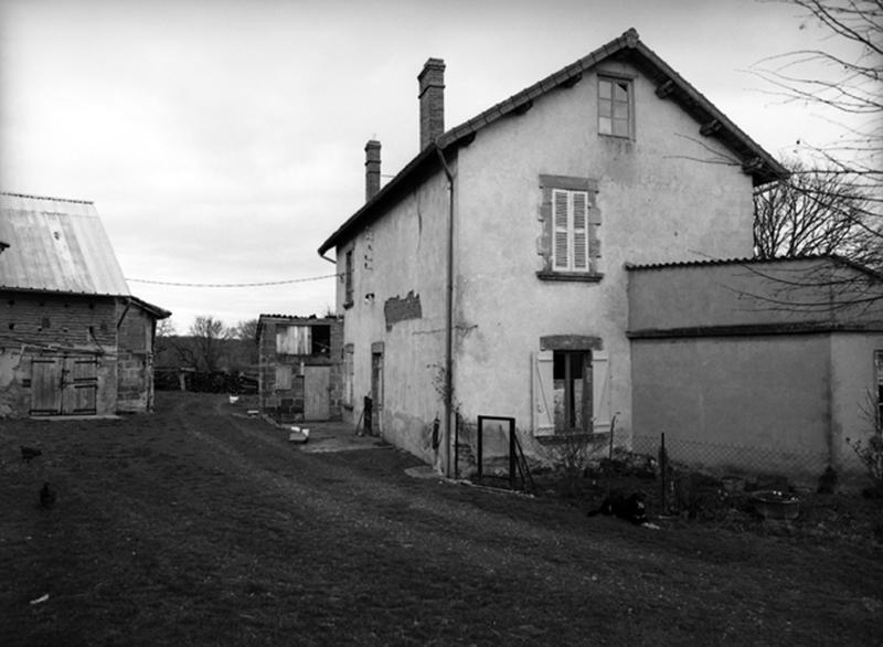 Vue de trois quarts du logis principal édifié en pisé, encadré de la resserre et d'une souillarde.