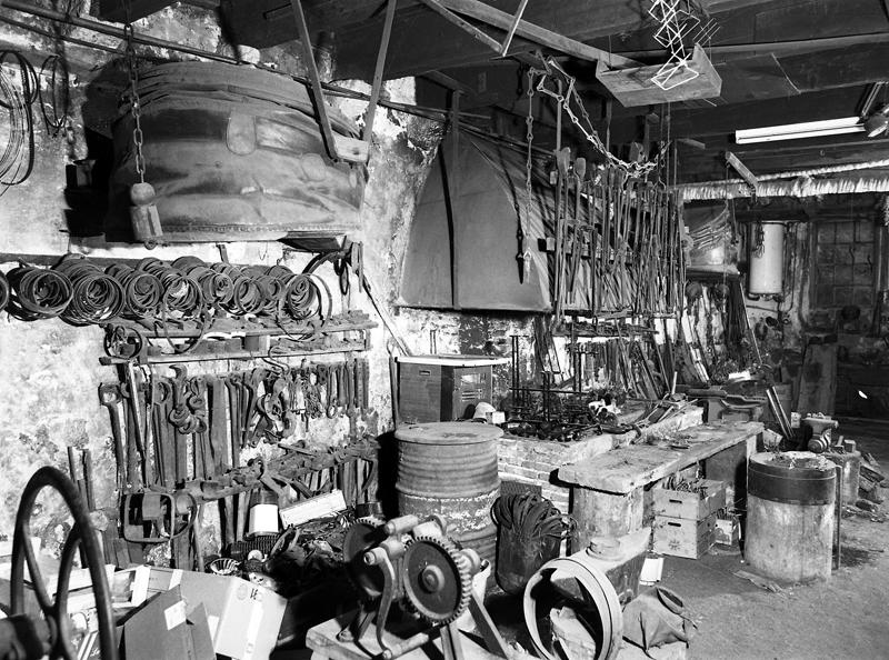 La forge : vue générale de trois quarts gauche avec cercles de moyeux de roues et outils.