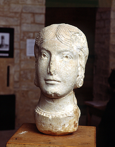 Tête féminine sculptée à l'époque romane dans un fragment de marbre antique déjà travaillé.