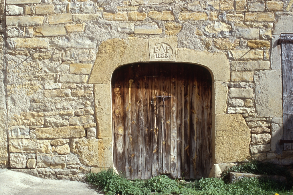 Porte charretière : inscription datée (1884) et emblème d'artisan maçon à la clef