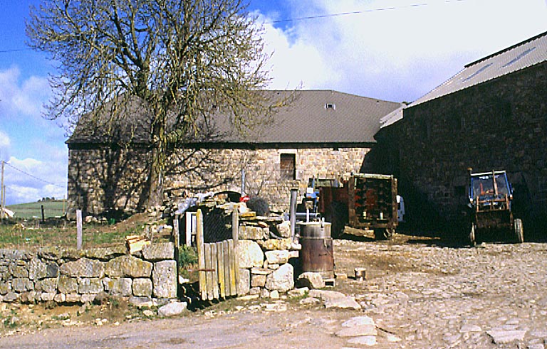 Vue d'ensemble de la cour avec en premier plan l'entrée de l'enclos et à l'arrière plan une grange-étable