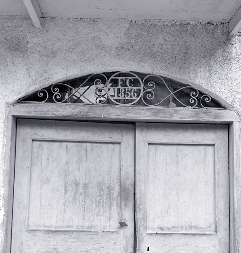 Maison 316. Façade antérieure sud. Porte d'entrée. Imposte en fer forgé. Monogramme découpé : FC - 1856. ; Le Fontenil. Parcelle 316. Façade sud. Porte d'entrée. Imposte en fer forgé. Monogramme découpé : FC 1856.