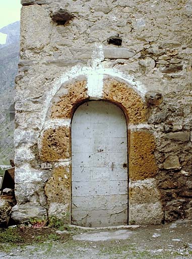 Chambre ménagère. La porte d'entrée. Le chambranle en tuf est souligné de blanc et surmonté d'une croix et la menuiserie recouverte de tôle.