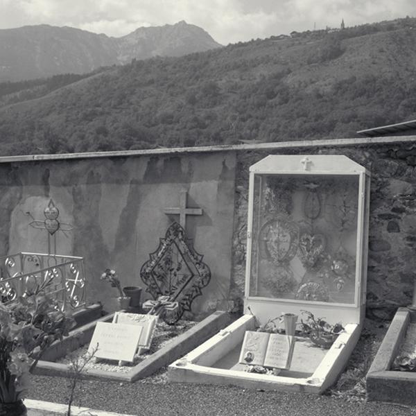 Le cimetière. Une tombe d'enfant datée 1956. Nombreuses couronnes de perles protégées par une vitrine dont les montants sont peints en blanc.