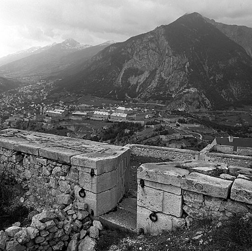 Vue prise du flanc gauche de la batterie supérieure du donjon vers le nord. Au premier plan, parapet et embrasure à canon avec, en contrebas, les batteries attenantes 45-46 et 43-42 et la toiture du corps de garde I (supérieur du Pont Rouge). Au deuxième plan, le fort des Têtes et, au fond, le fort des Salettes au pied du massif de la Croix de Toulouse.