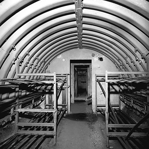 Intérieur. Local 7 : chambre de troupe. A droite et à gauche, des lits métalliques à étages, au fond, local 6 : chef de poste.