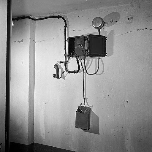 Ouvrage E. Poste téléphonique mural modèle 1932/RF, boîtier étanche ouvert. Au-dessus, sonnerie d'appel. En dessous, boîte à piles. A gauche, combiné.