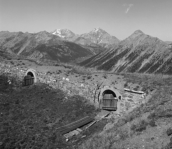 Batterie supérieure du cavalier, positions des pièces, vue prise vers le nord-est. Au premier plan, mur de revers du parapet et débouché des gaines d'aération des casemates A. Au fond, au centre, montagne et fort du Chaberton, dominant le village du Montgenèvre, et, à droite, sommet de Château-Jouan masquant le fort du Janus.