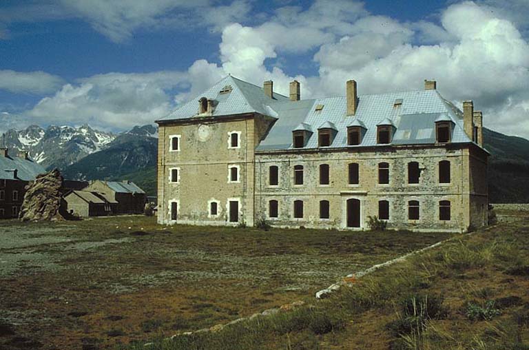 Cour centrale. Bâtiment E (ancienne chapelle) et pavillon D (gouvernement). A l'arrière plan, à gauche, la caserne K, le garage P et le bâtiment R. Le rocher à gauche du bâtiment E, vestige du relief originel, aurait dû être rasé pour faire place à un bâtiment projeté, mais non construit.