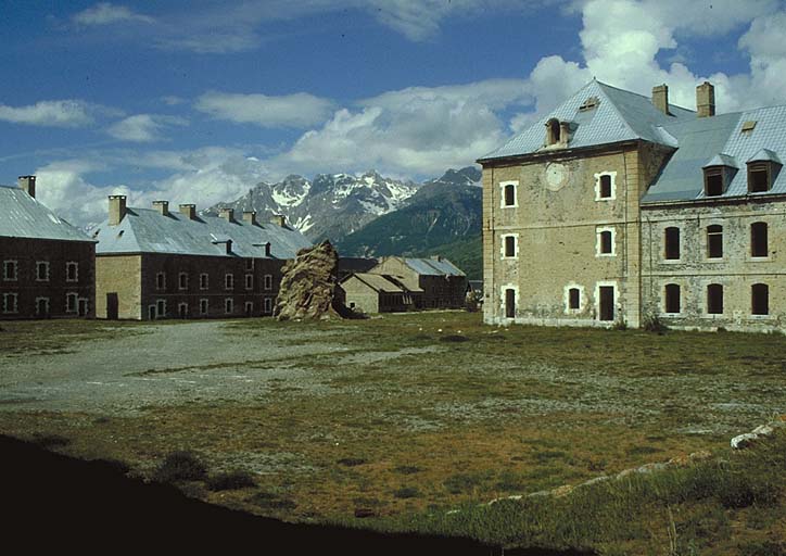 Cour centrale. Bâtiment E (ancienne chapelle) et pavillon D (gouvernement). A l'arrière plan, à gauche, la caserne K, le garage P et le bâtiment R. Le rocher à gauche du bâtiment E, vestige du relief originel, aurait dû être rasé pour faire place à un bâtiment projeté, mais non construit.