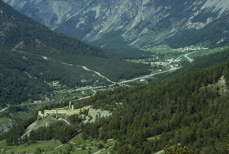 Vue lointaine du fort prise du fort du Randouillet, à 1000 m au sud. Au centre, vallon de Fontenil avec à droite le fort et, à gauche, le saillant de tête du fort des Têtes, dominé, en arrière plan, par le fort des Salettes. Au fond, vallée de la Durance et route du Montgenèvre.