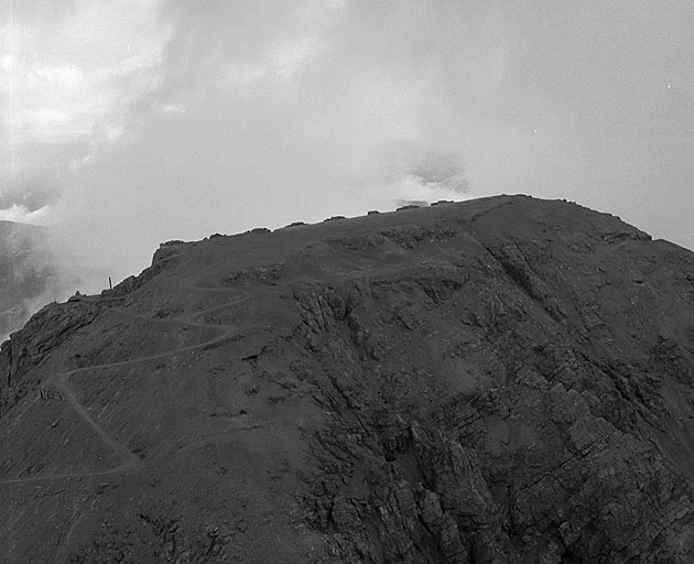 Vue aérienne prise de l'ouest. On aperçoit le sommet des tours supports des tourelles de 149 en partie défilées par le masque rocheux naturel arasé en glacis. A gauche, derniers lacets supérieurs de la route d'accès.