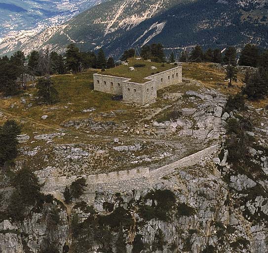 Vue aérienne du blockhaus prise du sud-sud-est. Au second plan, au-delà de la vallée de la Cerveyrette, la crête jalonnée de gauche à droite par l'Infernet, la Cochette, l'Ombilic, le plateau du Gondran avec, derrière, le Janus.