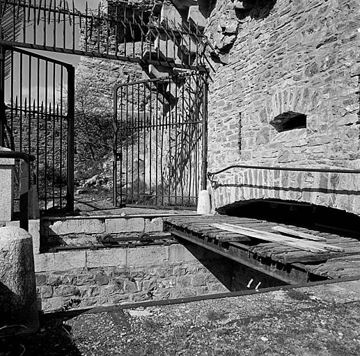 Fort supérieur. Front de tête. Porte. Vue rapprochée prise de l'extérieur. Au premier plan, le haha coupant la route et le pont roulant en partie effacé dans sa casemate. Derrière, grille défensive et avant-porte. A l'arrière-plan, double caponnière.