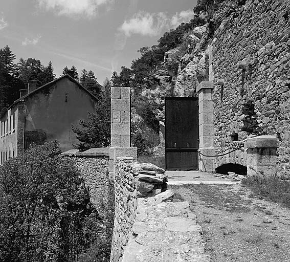 Porte inférieure. Au premier plan, à gauche, mur de soutènement bordant le ravin. A droite, escarpe du front est et arcature d'effacement du pont roulant de la porte. En arrière, à gauche, caserne.