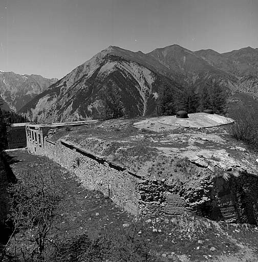 Dessus de l'ouvrage vu du sud, au-dessus des blocs 2 et 3. Au premier plan, le fossé (reliquat de l'ancienne redoute) avec, à l'angle, l'emplacement de la caponnière double et le bouchon en béton de la galerie d'accès. Derrière, le bloc 4 (observatoire cuirassé).