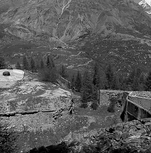 Vue prise du haut du bloc 3, dans l'axe du fossé du front de tête. A gauche, le bloc 4 (observatoire cuirassé). Au fond, le village de Saint-Ours avec, à l'extrême droite, l'ouvrage haut de Saint-Ours. A droite, haut du bloc 2.