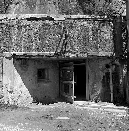 Bloc 1. Vue de face. Façade avec la porte d'entrée et l'arrivée de la voie de 0,60 venant du téléphérique. A gauche, caponnière et créneau de FM de défense rapprochée. Au-dessus, visière et supports de l'antenne radio.